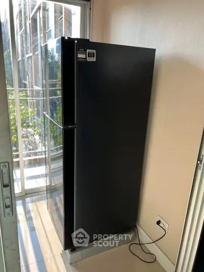 Modern black refrigerator in a bright room with glass doors and outdoor view.