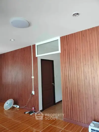 Modern interior with wood panel walls and tiled flooring, featuring a closed door and ceiling lights.