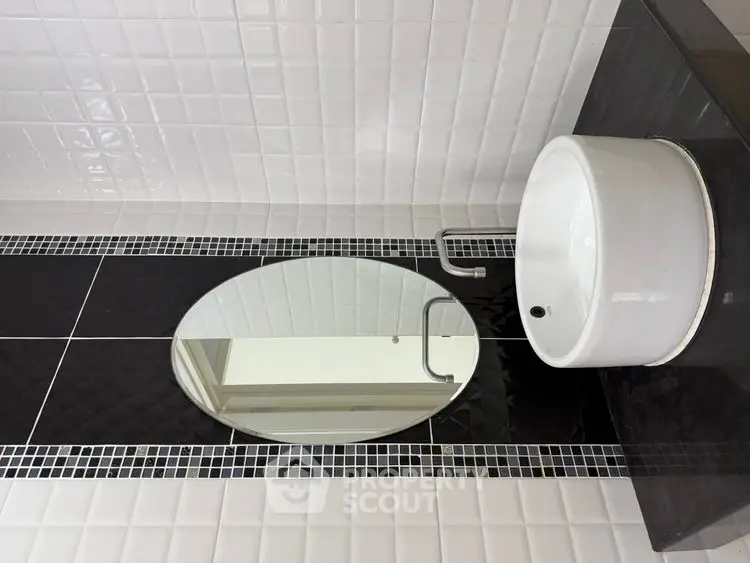Modern bathroom with stylish black and white tile design and sleek round sink.