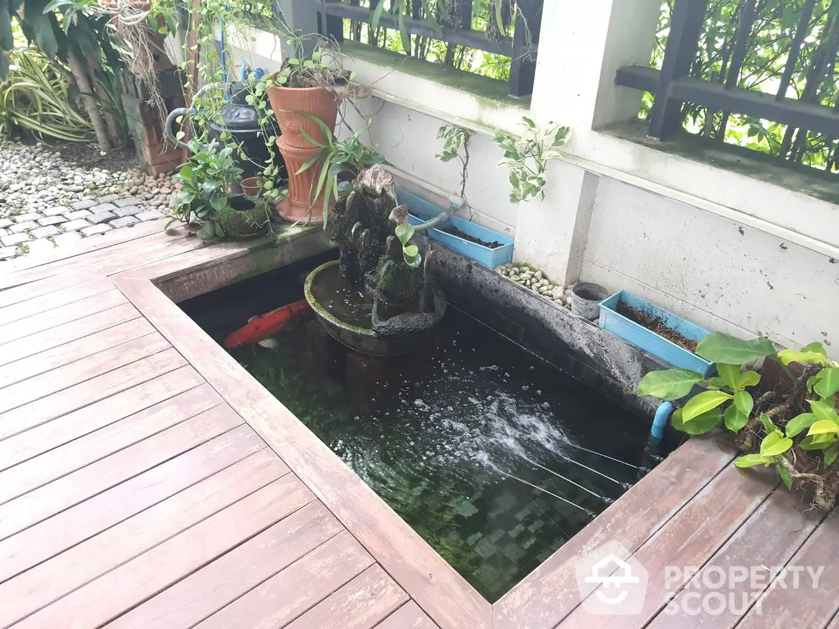 Charming outdoor space featuring a tranquil fish pond with a fountain, surrounded by lush greenery and a wooden deck, perfect for relaxation.