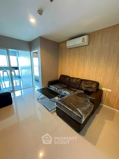 Modern living room with sleek black sofa and glass coffee table, featuring a stylish wood accent wall and air conditioning.