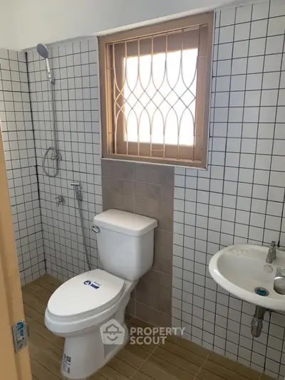 Modern bathroom with tiled walls and window, featuring a toilet and sink.