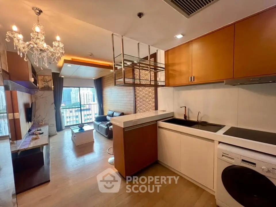 Modern open-layout living room with kitchen, featuring elegant chandelier and city view balcony.