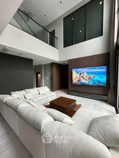 Luxurious modern living room with high ceiling and large TV, featuring elegant white sectional sofa.