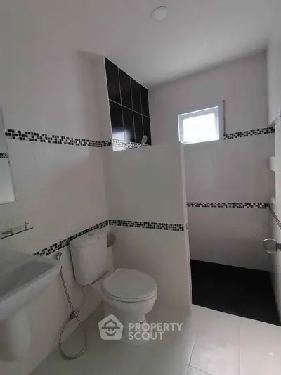 Modern bathroom with sleek black and white tiles, featuring a toilet and shower area.