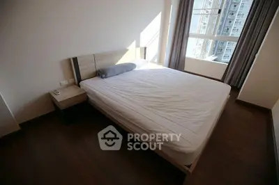 Spacious bedroom with large window and modern furnishings in a high-rise apartment.