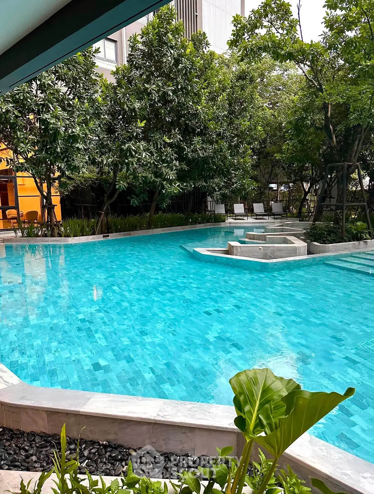 Luxurious outdoor pool surrounded by lush greenery in a modern residential complex.