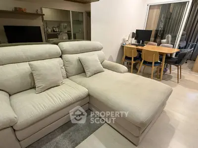 Spacious living room with modern beige sectional sofa and dining area in open layout apartment.