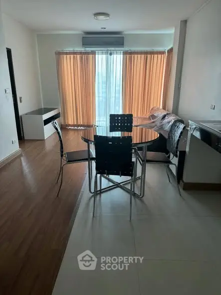 Modern dining area with glass table and stylish chairs, featuring large windows and wooden flooring.