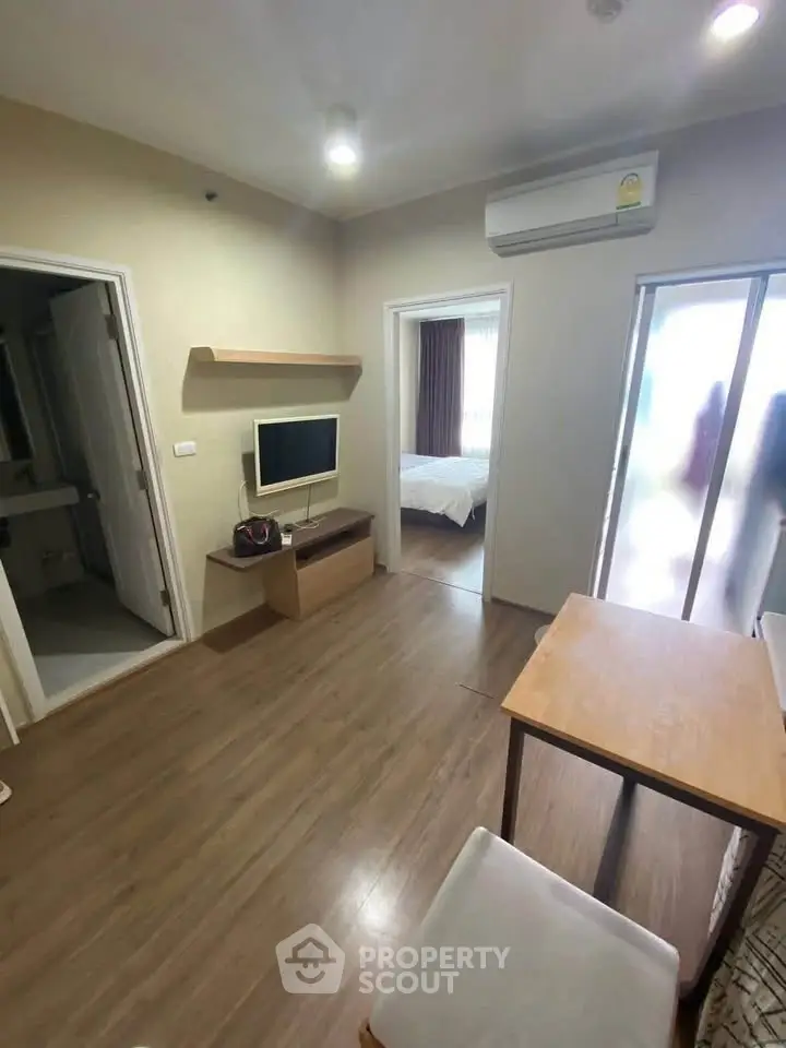 Modern apartment interior with wooden flooring, TV, and air conditioning, leading to a cozy bedroom.