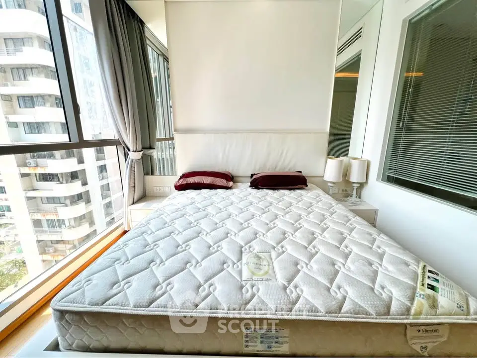 Modern bedroom with large windows and city view, featuring a comfortable bed and stylish decor.