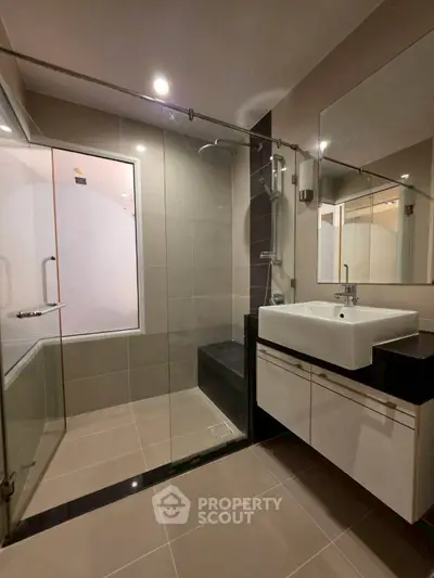 Modern bathroom with glass shower and sleek vanity in contemporary apartment.