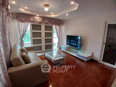 Spacious living room with elegant decor and large TV, featuring parquet flooring and natural light.