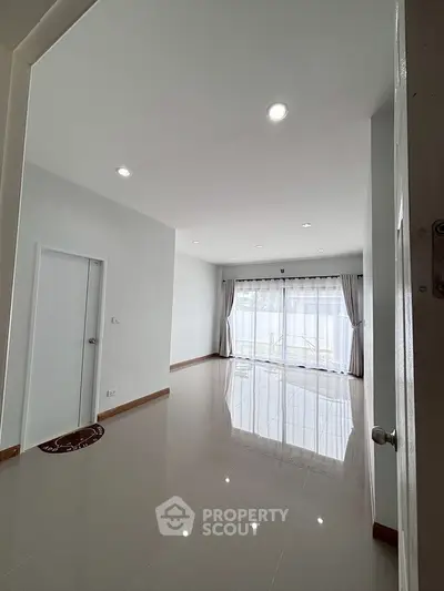 Spacious empty room with glossy tiled floor and large window for natural light.
