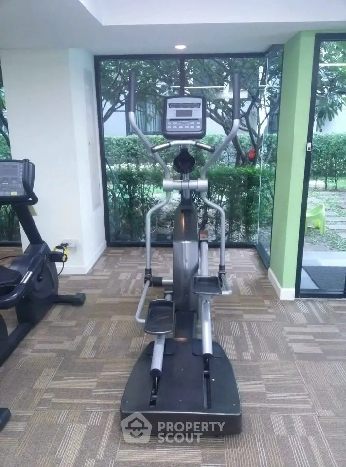 Modern gym with elliptical machine and garden view in luxury apartment complex.