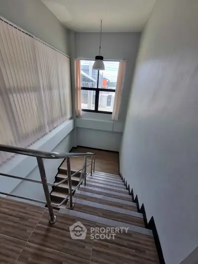 Modern staircase with sleek metal railing and large window, offering natural light and contemporary design.