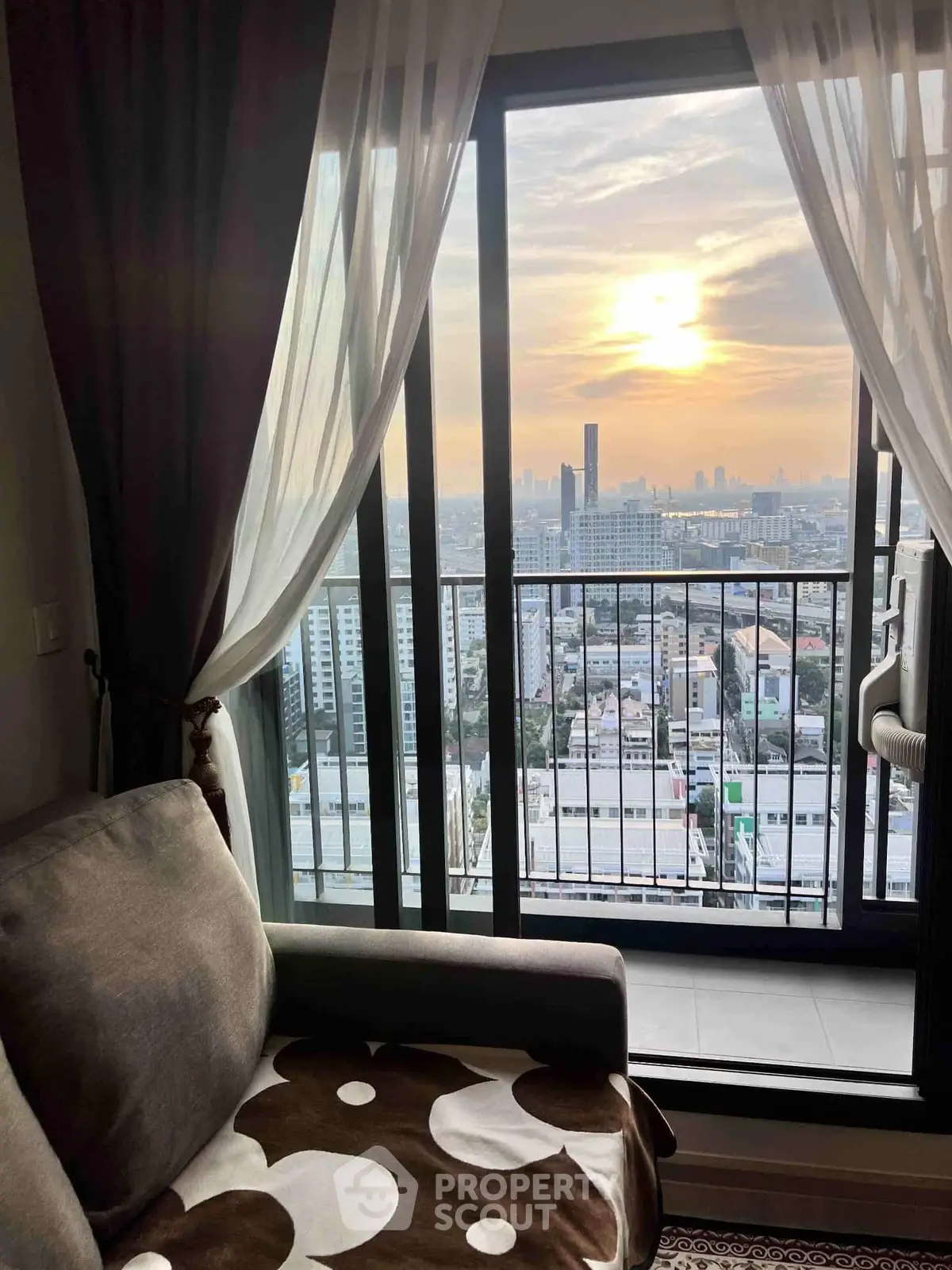 Stunning city view from a cozy living room with floor-to-ceiling windows and elegant curtains.