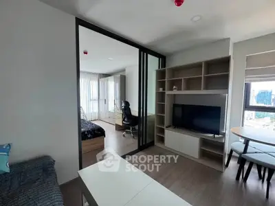Modern apartment living room with TV, sliding doors to bedroom, and city view.