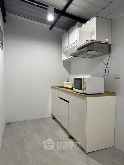 Modern minimalist kitchen with sleek cabinets and microwave on countertop.