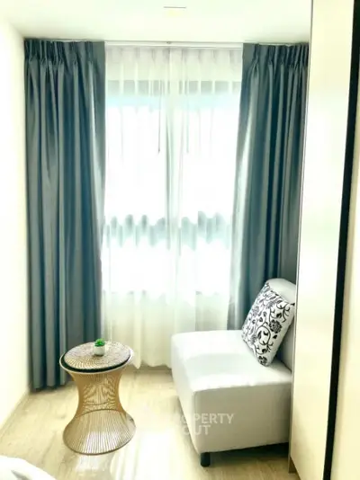 Sunlit cozy corner with elegant blue drapes and a chic white chaise, accented by a stylish cushion and a unique side table.