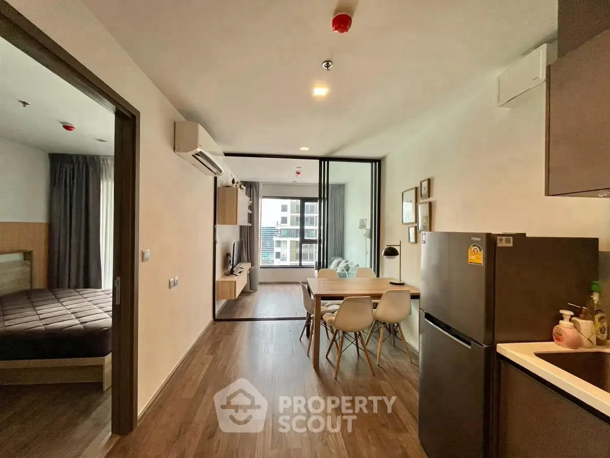 Modern open-plan apartment with sleek kitchen and cozy living area, featuring stylish dining set and spacious bedroom.