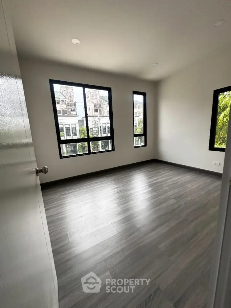 Spacious empty room with large windows and modern flooring in urban apartment.