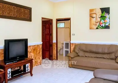 Cozy living room with leather sofas and TV, adjacent to a bathroom.