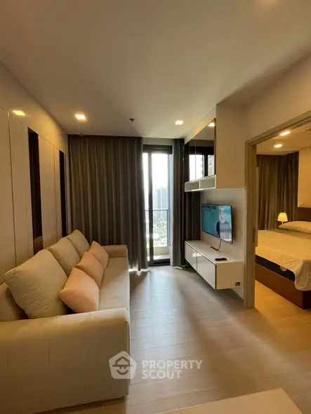 Modern living room with cozy sofa and TV, leading to a bedroom with a large window view.