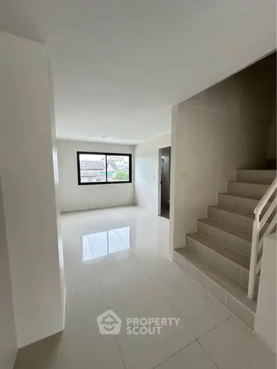 Spacious modern living room with large window and staircase, perfect for family gatherings.