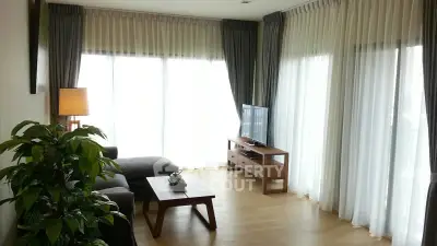 Spacious living room with large windows and elegant curtains, featuring modern furniture and a cozy ambiance.