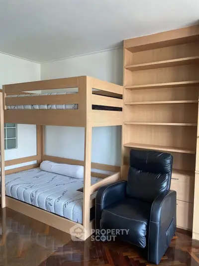 Cozy bedroom with bunk bed, armchair, and built-in shelving for optimal space utilization.