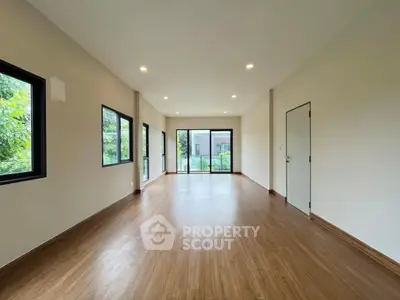 Spacious empty room with large windows and wooden flooring, ideal for customization.