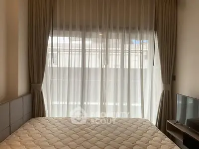 Cozy bedroom with large window and elegant curtains, featuring a comfortable bed and modern TV setup.