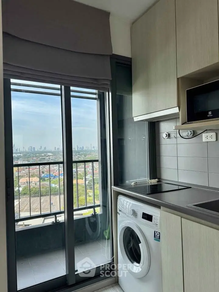 Modern kitchen with washing machine and city view from balcony in high-rise apartment.