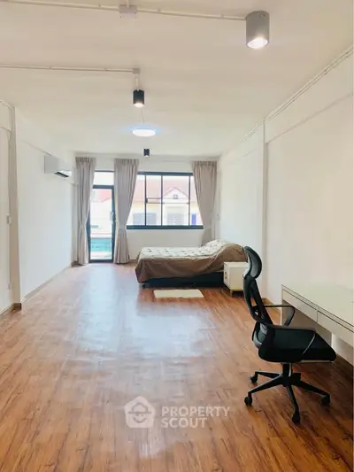 Spacious bedroom with wooden flooring and large window offering natural light.
