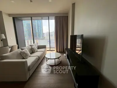 Modern living room with large windows and city view, featuring a comfortable sofa and sleek TV setup.