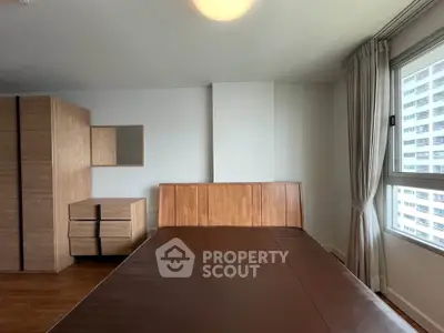 Spacious bedroom with wooden furniture and large window offering natural light.