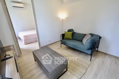Cozy living room with modern furniture and natural light, leading to a serene bedroom.