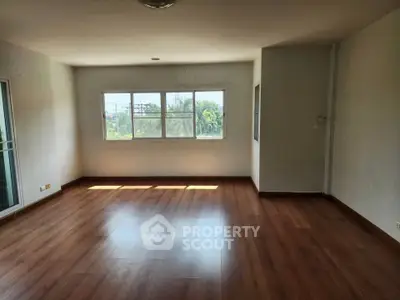 Spacious empty room with wooden flooring and large windows offering natural light.