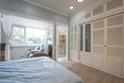 Spacious bedroom with large windows and cozy seating area, featuring elegant built-in closets.