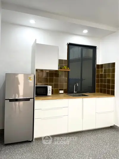 Modern kitchen with sleek white cabinets, stainless steel fridge, and stylish backsplash.