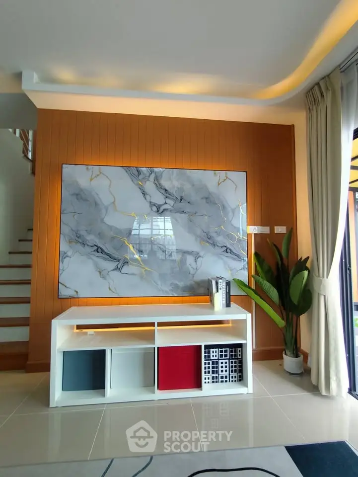 Modern living room with stylish decor and elegant staircase, featuring a large marble artwork and sleek storage unit.