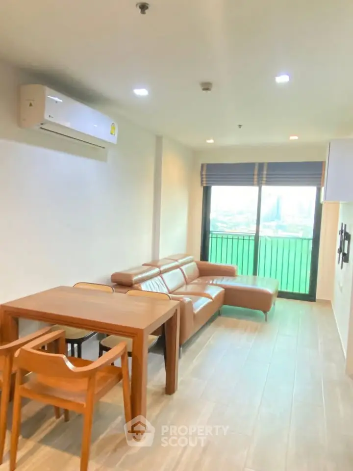 Modern living room with leather sofa and dining set, featuring large window with city view.