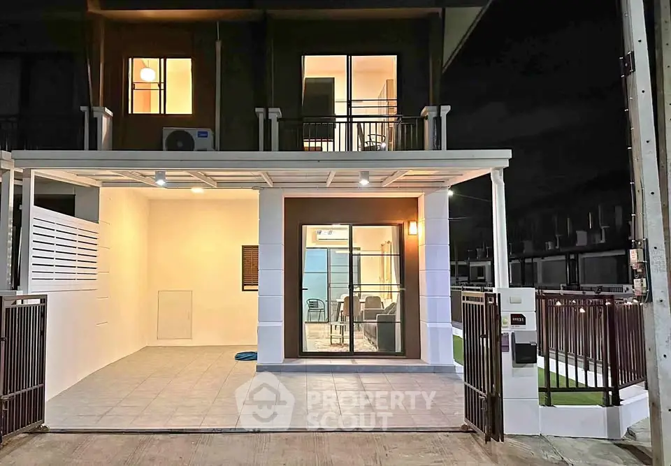 Modern two-story townhouse with illuminated facade and spacious carport at night.