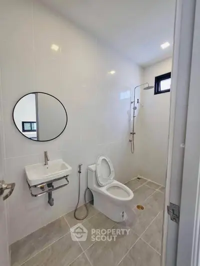 Modern minimalist bathroom with sleek fixtures and neutral tiles, featuring a round mirror and compact sink.