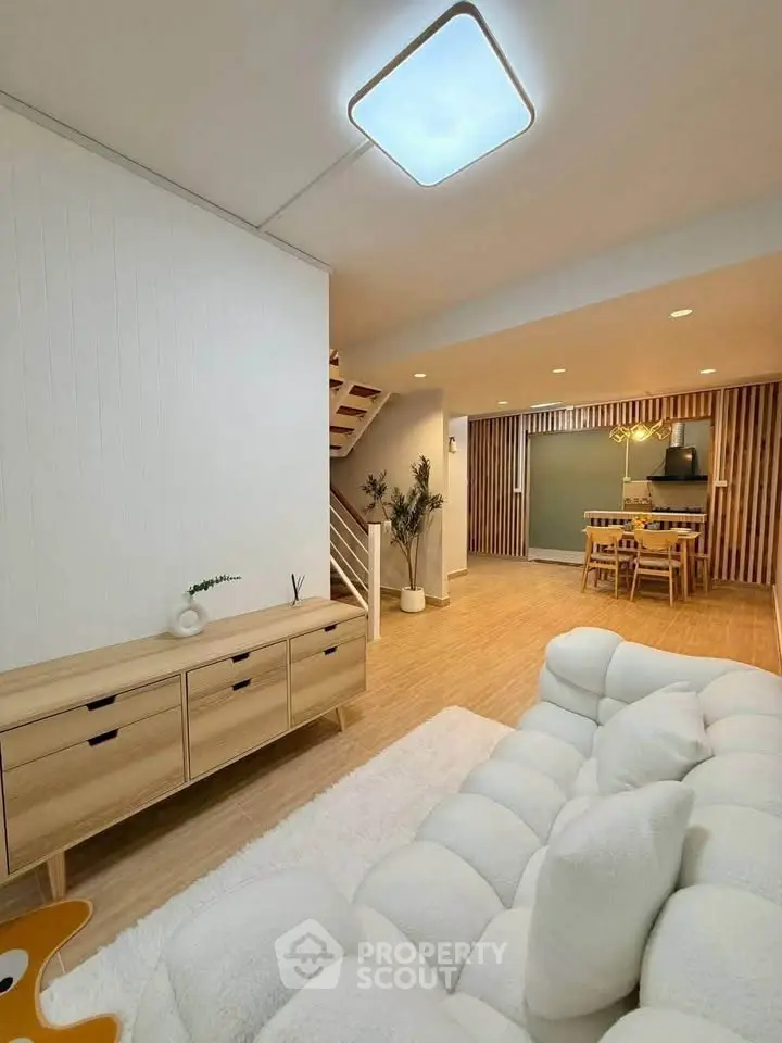 Spacious modern living room with cozy white sofa and elegant wooden dining area, perfect for family gatherings.