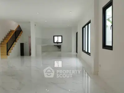 Spacious modern living room with marble flooring and open kitchen layout, featuring large windows and a sleek staircase.