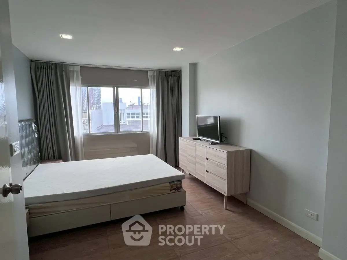 Modern bedroom with large window and city view, featuring a bed, TV, and dresser in a minimalist design.