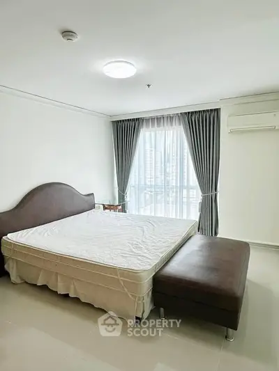 Spacious bedroom with large window and modern furnishings in a high-rise apartment.