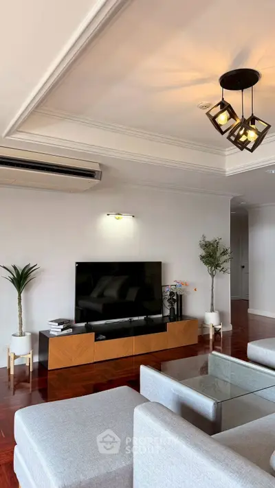 Spacious living room with modern decor and elegant lighting, featuring a large TV and stylish furniture.
